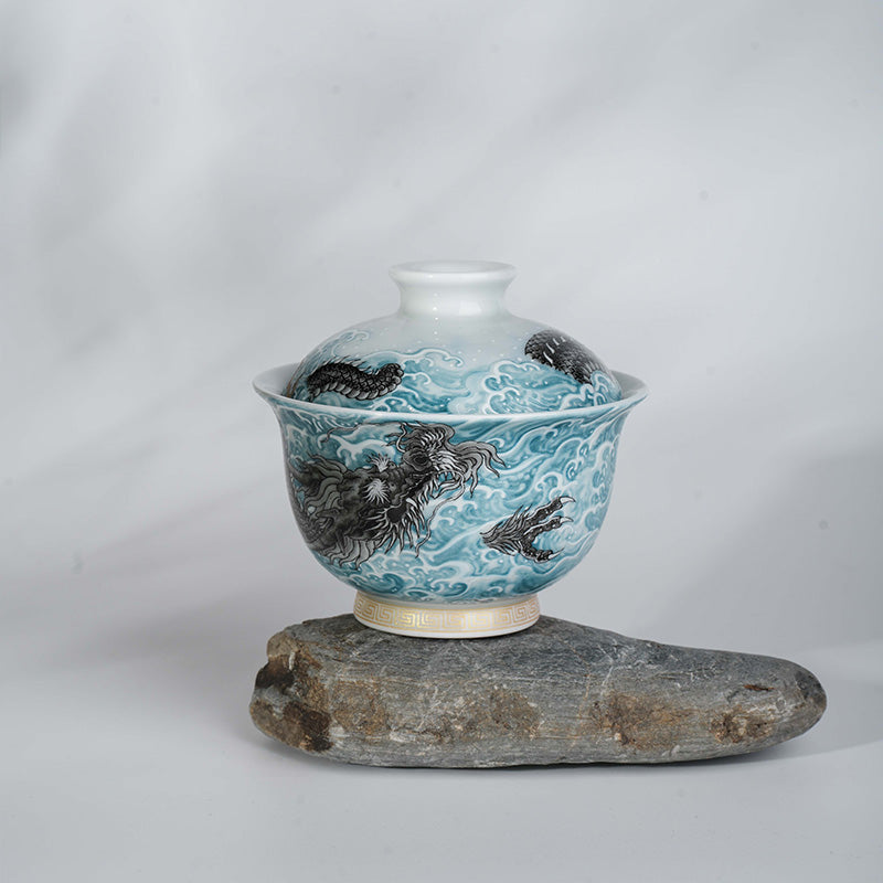 This showcases an exquisite blue and white gaiwan with a lifelike loong pattern. The bowl is placed on an irregular gray stone base with a light background, creating a classic and elegant atmosphere.