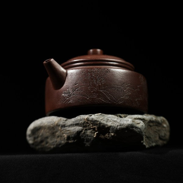 This purple clay teapot is dark brown in color, with a Chinese garden landscape of a small bridge and flowing water painted on the left side of the teapot, and the words "Sitting and Drinking Tea" engraved on the right side. This purple clay teapot was made by Chinese purple clay teapot master Chen Xiaozhong and was produced in Yixing, a famous purple clay teapot production area in China.