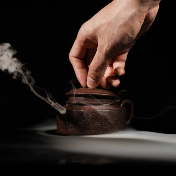 This purple clay teapot is dark brown in color, with a Chinese garden landscape of a small bridge and flowing water painted on the left side of the teapot, and the words "Sitting and Drinking Tea" engraved on the right side. This purple clay teapot was made by Chinese purple clay teapot master Chen Xiaozhong and was produced in Yixing, a famous purple clay teapot production area in China.