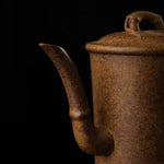 This shows a purple clay teapot with a brown body in the shape of a bamboo joint, a short spout, a curved handle, and bamboo leaf carvings on the body. It is placed on an irregularly shaped stone base.