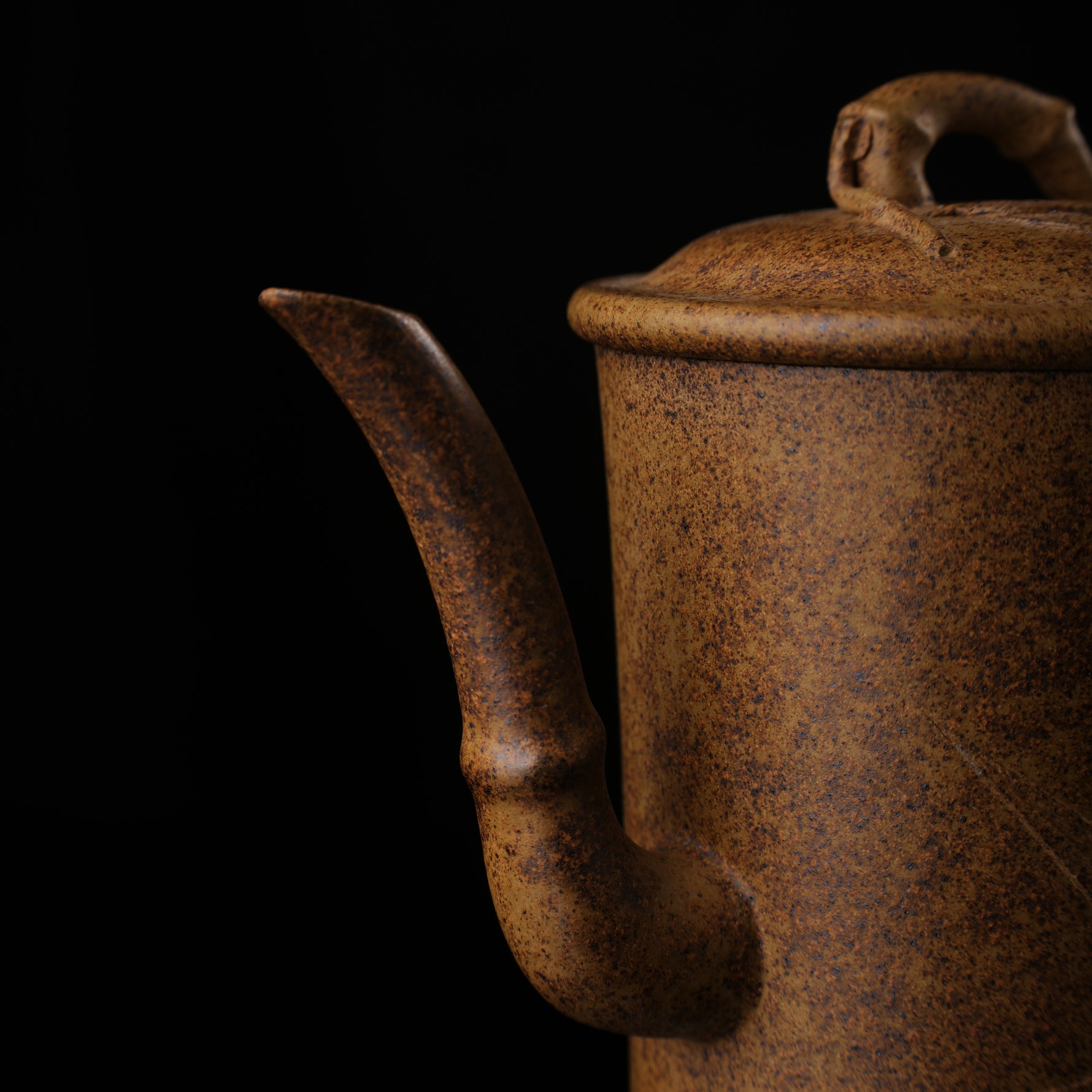 This shows a purple clay teapot with a brown body in the shape of a bamboo joint, a short spout, a curved handle, and bamboo leaf carvings on the body. It is placed on an irregularly shaped stone base.