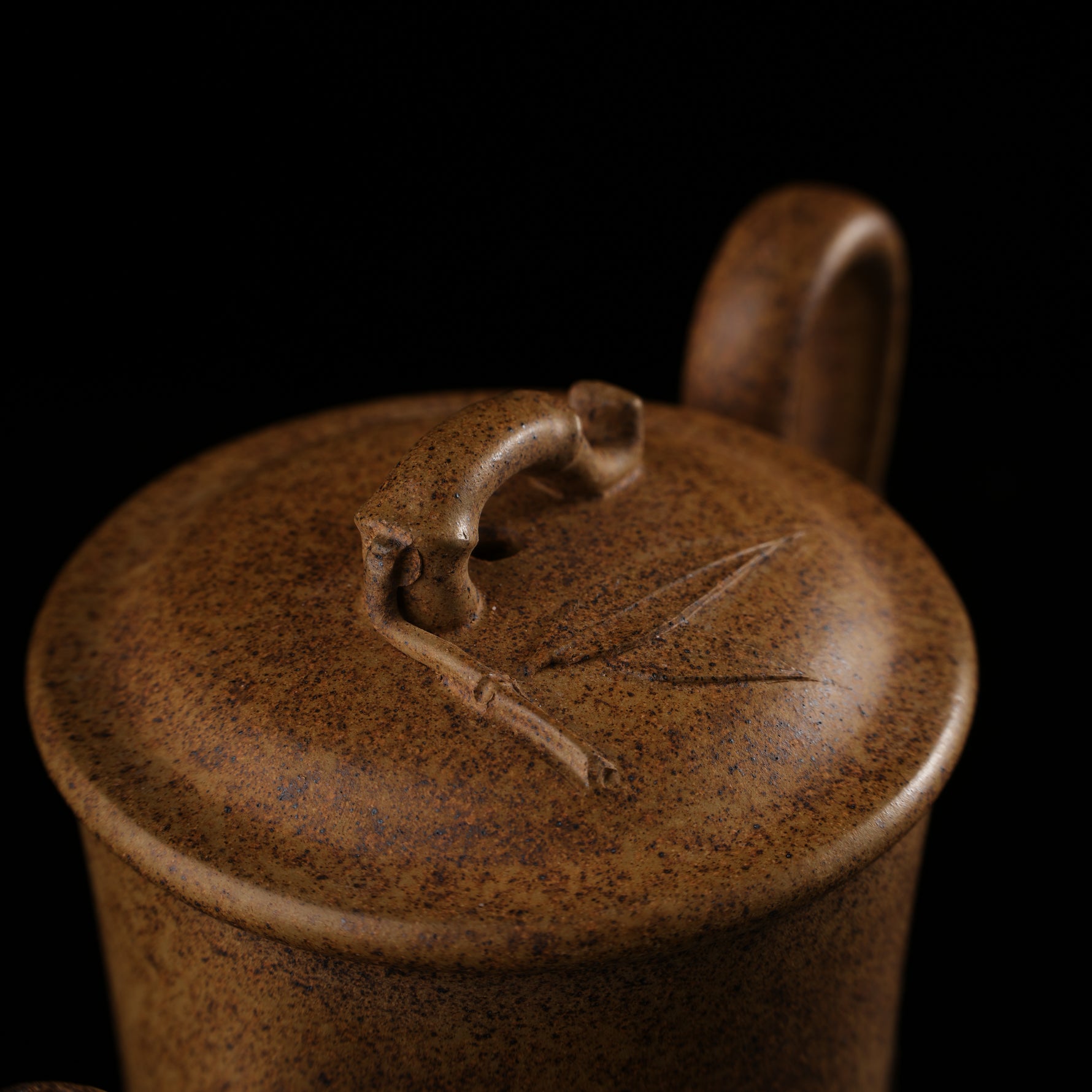 This shows a purple clay teapot with a brown body in the shape of a bamboo joint, a short spout, a curved handle, and bamboo leaf carvings on the body. It is placed on an irregularly shaped stone base.