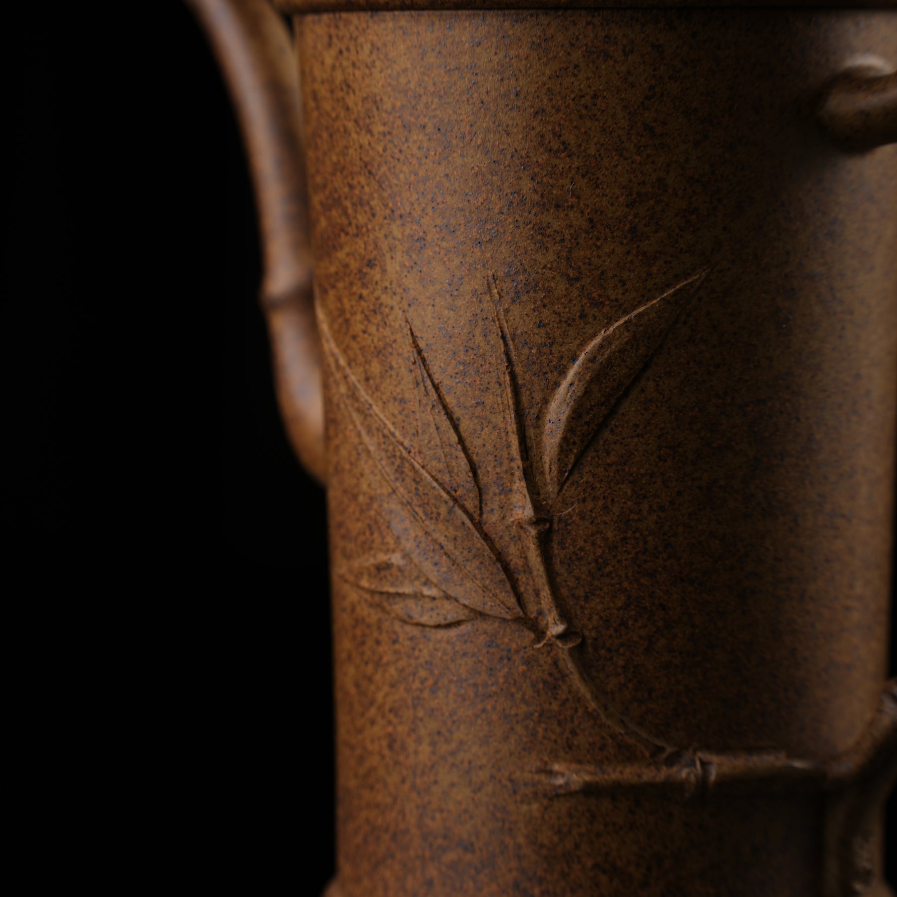 This shows a purple clay teapot with a brown body in the shape of a bamboo joint, a short spout, a curved handle, and bamboo leaf carvings on the body. It is placed on an irregularly shaped stone base.