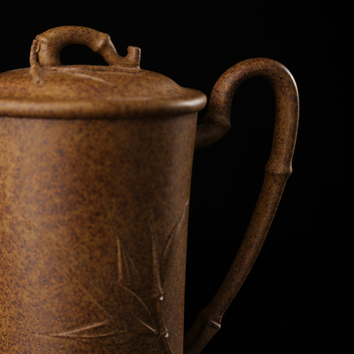 This shows a purple clay teapot with a brown body in the shape of a bamboo joint, a short spout, a curved handle, and bamboo leaf carvings on the body. It is placed on an irregularly shaped stone base.