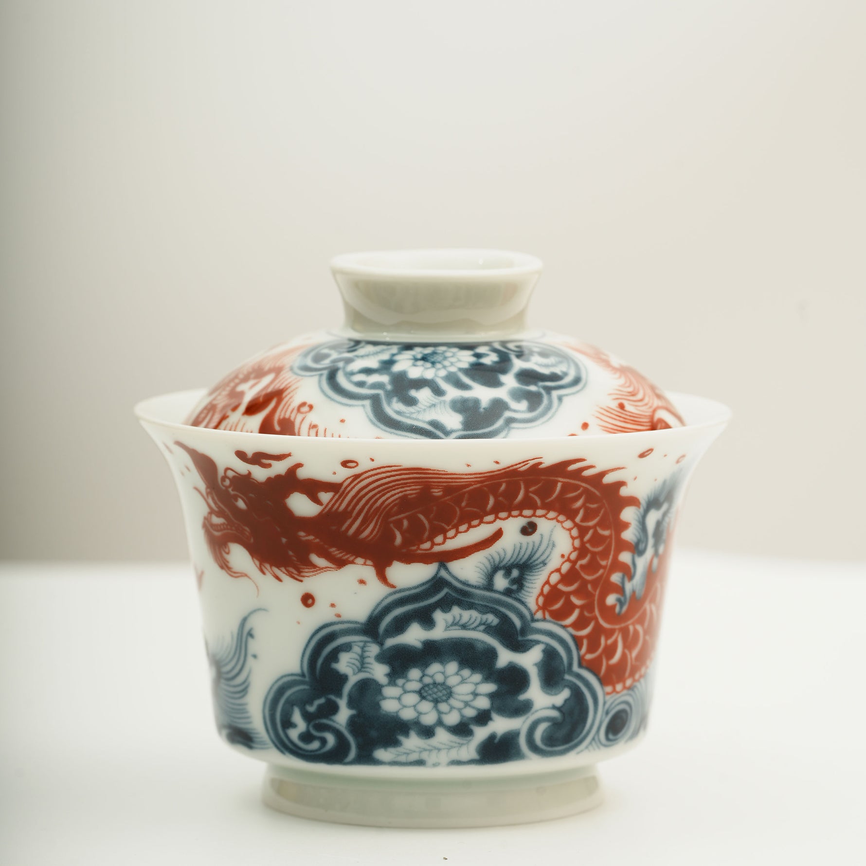 The Gaiwan has a white base with blue and white wave patterns on it, and a red Chinese loong is flying above the waves.
