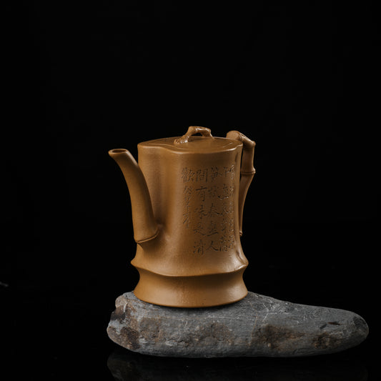 This shows a purple clay teapot with a warm yellow body, engraved with words, a short spout, a well-curved handle, and a tightly fitting lid. The purple clay teapot is placed on a gray irregular-shaped base.