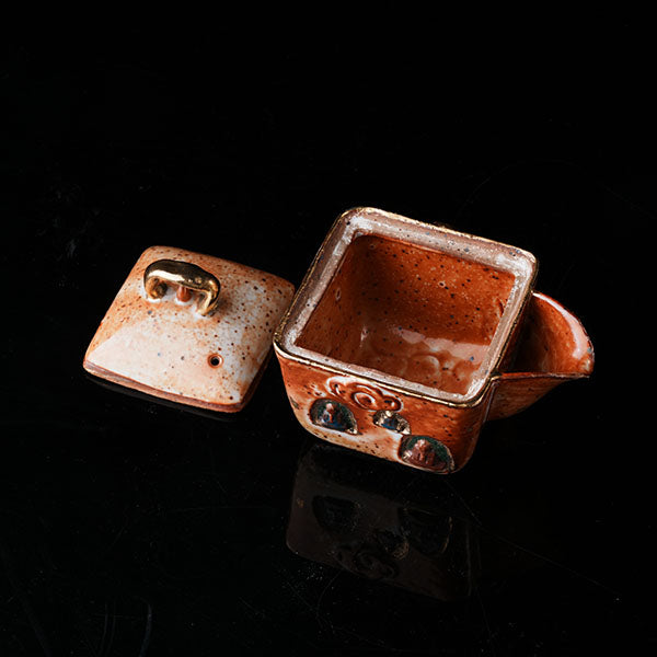 The Buddha without Form Square Teapot - Traditional ceramic teapot with square form, speckled brown glaze, gold handle, and relief figures (possibly Buddhist motifs). Handcrafted, rustic design, ideal for tea rituals. Features intricate detailing, cultural artistry, and functional elegance. Perfect for collectors of unique teaware, highlighting craftsmanship and traditional aesthetics.