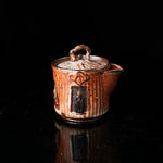 A traditional ceramic teapot with a rustic, speckled brown-orange glaze. It features a lid with a handle, a meditating figure relief, and intricate textural designs. Ideal for tea ceremonies, embodying Asian art and mindfulness. Handcrafted, showcasing cultural heritage and artistic detail. Perfect for collectors of unique teaware, highlighting traditional craftsmanship and spiritual motifs. 