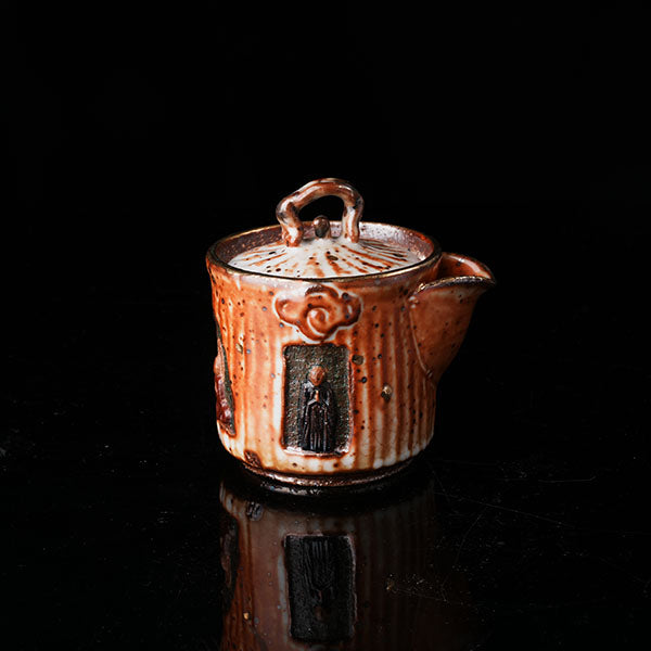 A traditional ceramic teapot with a rustic, speckled brown-orange glaze. It features a lid with a handle, a meditating figure relief, and intricate textural designs. Ideal for tea ceremonies, embodying Asian art and mindfulness. Handcrafted, showcasing cultural heritage and artistic detail. Perfect for collectors of unique teaware, highlighting traditional craftsmanship and spiritual motifs. 