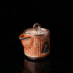 A traditional ceramic teapot with a rustic, speckled brown-orange glaze. It features a lid with a handle, a meditating figure relief, and intricate textural designs. Ideal for tea ceremonies, embodying Asian art and mindfulness. Handcrafted, showcasing cultural heritage and artistic detail. Perfect for collectors of unique teaware, highlighting traditional craftsmanship and spiritual motifs. 