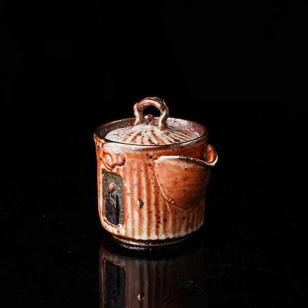 A traditional ceramic teapot with a rustic, speckled brown-orange glaze. It features a lid with a handle, a meditating figure relief, and intricate textural designs. Ideal for tea ceremonies, embodying Asian art and mindfulness. Handcrafted, showcasing cultural heritage and artistic detail. Perfect for collectors of unique teaware, highlighting traditional craftsmanship and spiritual motifs. 