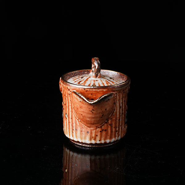 A traditional ceramic teapot with a rustic, speckled brown-orange glaze. It features a lid with a handle, a meditating figure relief, and intricate textural designs. Ideal for tea ceremonies, embodying Asian art and mindfulness. Handcrafted, showcasing cultural heritage and artistic detail. Perfect for collectors of unique teaware, highlighting traditional craftsmanship and spiritual motifs. 