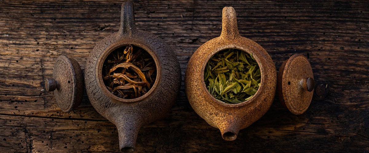 Two teapots, both filled with tea leaves. Lids placed on both sides.